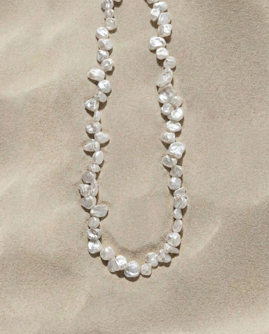 Full strand of white Keshi pearls arranged on a warm sand-textured background