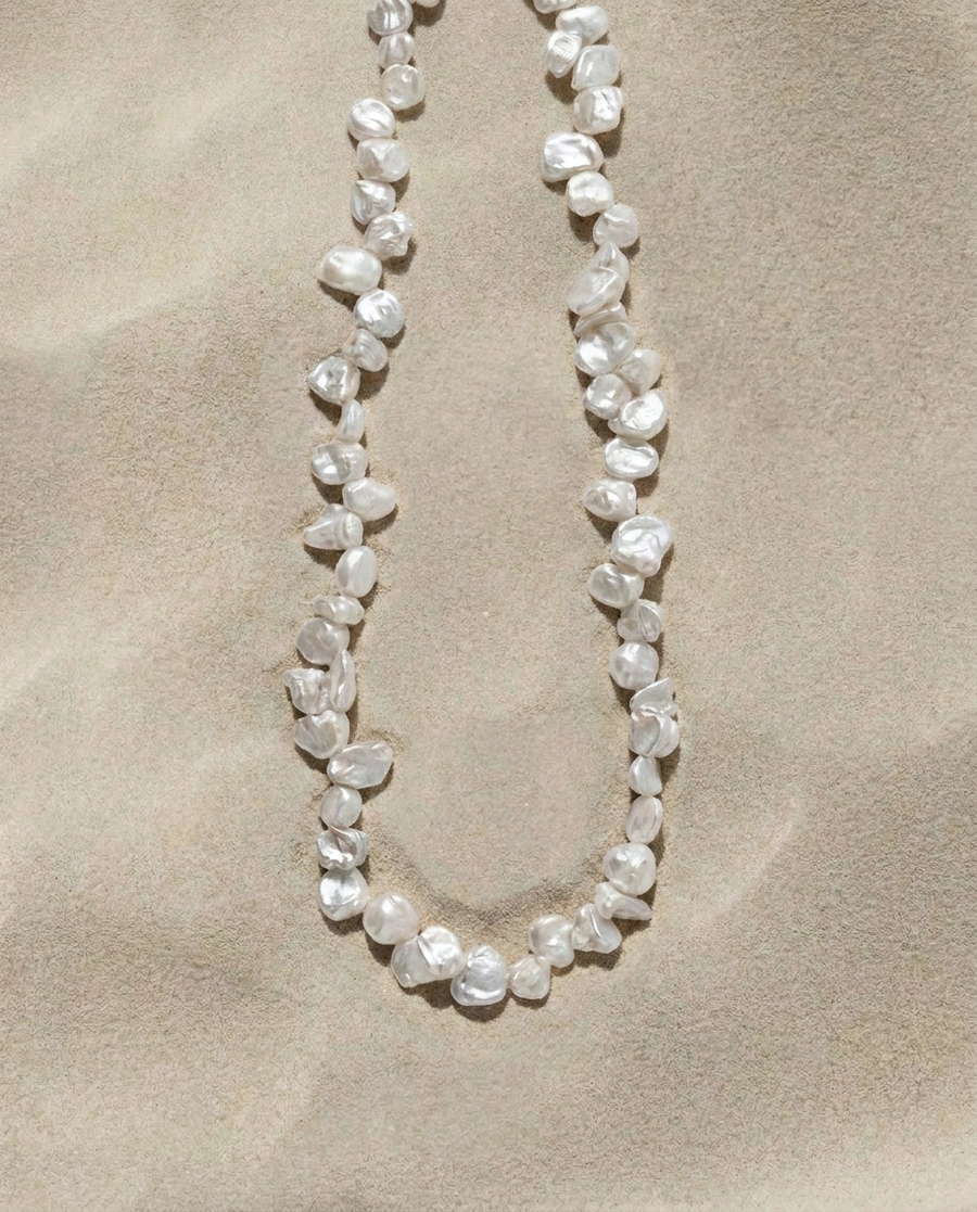 Full strand of white Keshi pearls arranged on a warm sand-textured background