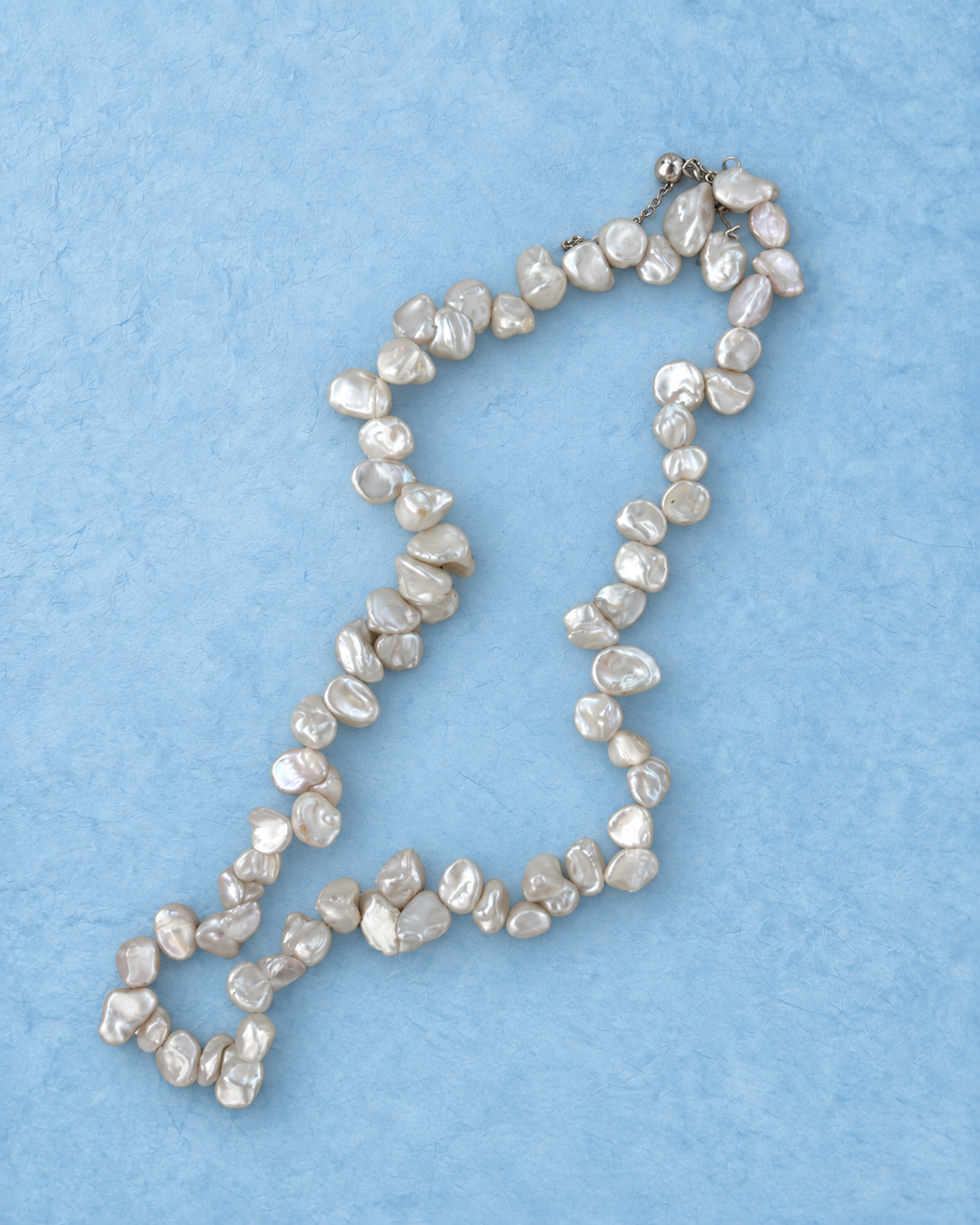 Ivory Nacre Loop Necklace on light blue background, curved arrangement