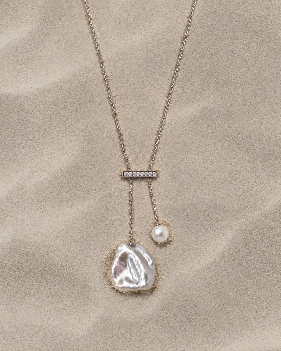Silver necklace with an asymmetric irregular pearl and round pearl on a sand-textured background