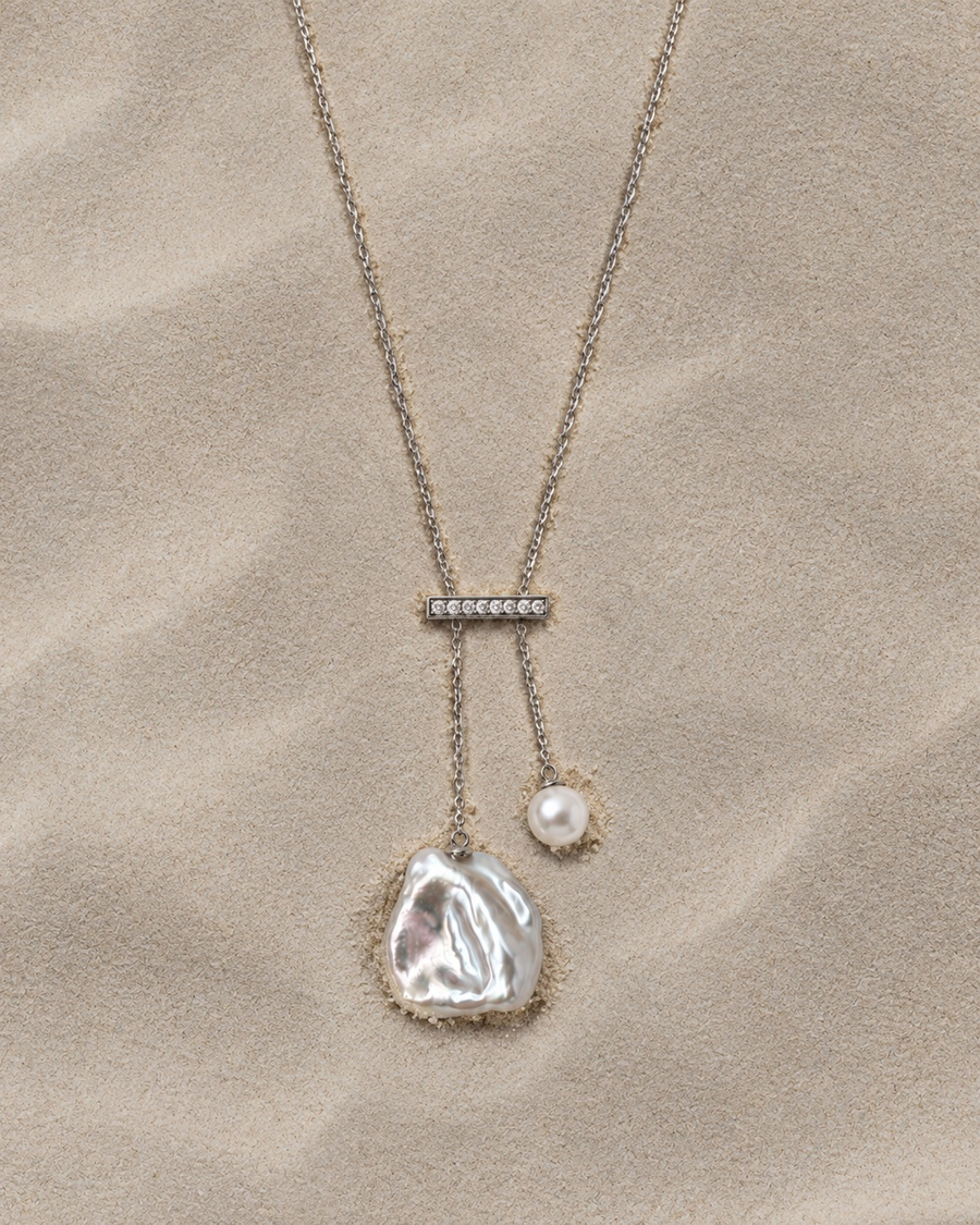 Silver necklace with an asymmetric irregular pearl and round pearl on a sand-textured background