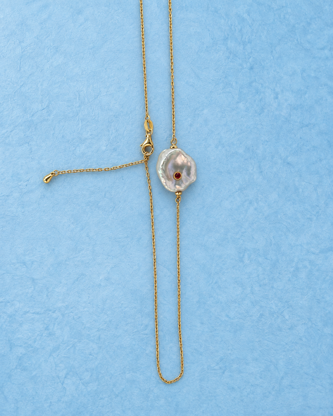 Calyra Necklace on light blue background, vertical arrangement