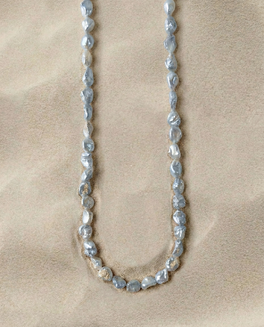 Full strand of irregular blue-silver pearls arranged on a warm sand-textured background