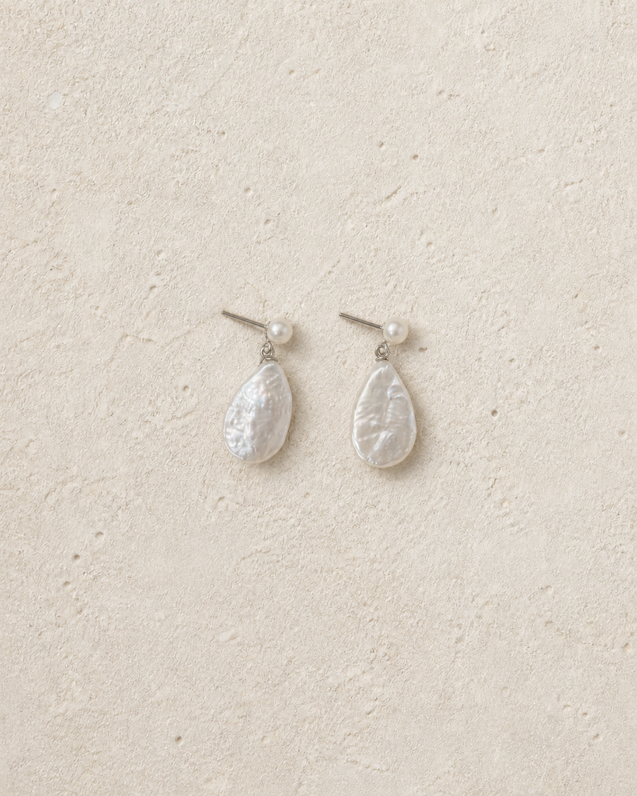 Lumen pearl drop earrings resting on warm ivory limestone