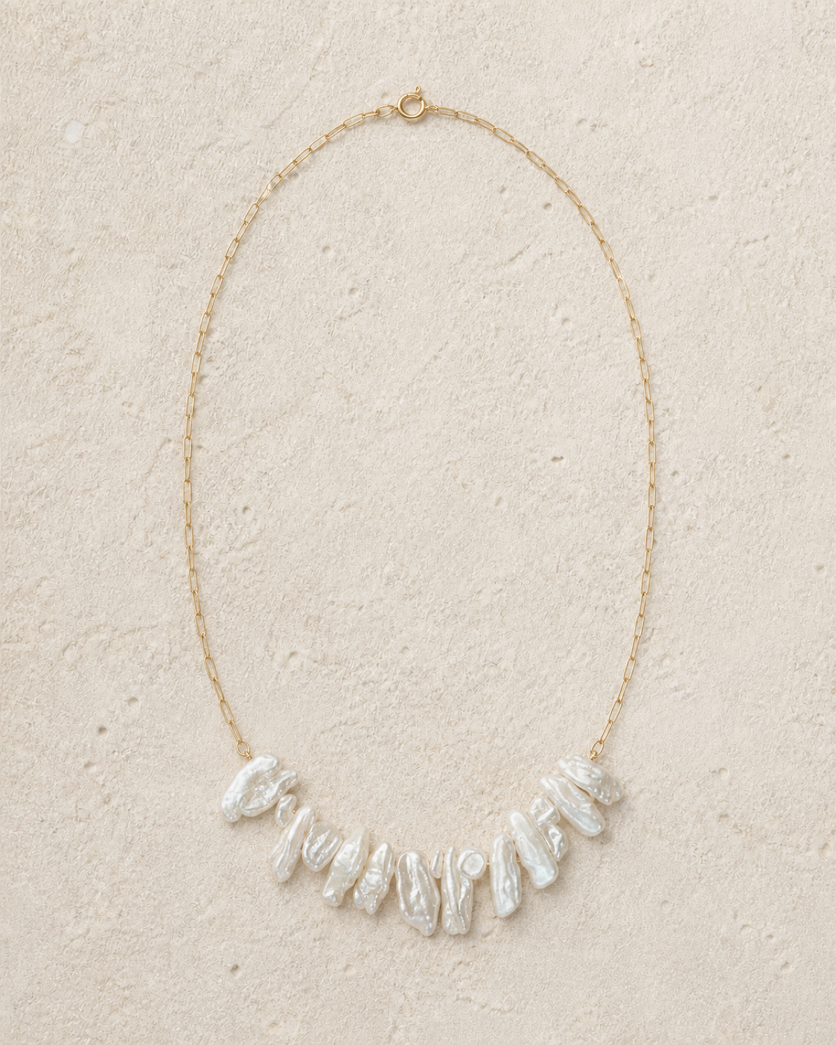 Crescent Biwa Pearl Necklace arranged in a naturally irregular crescent on warm ivory limestone