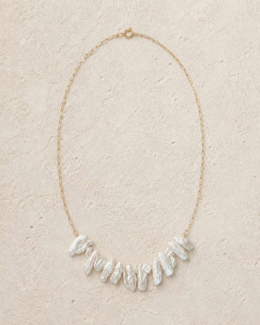 Crescent Biwa Pearl Necklace arranged in a naturally irregular crescent on warm ivory limestone