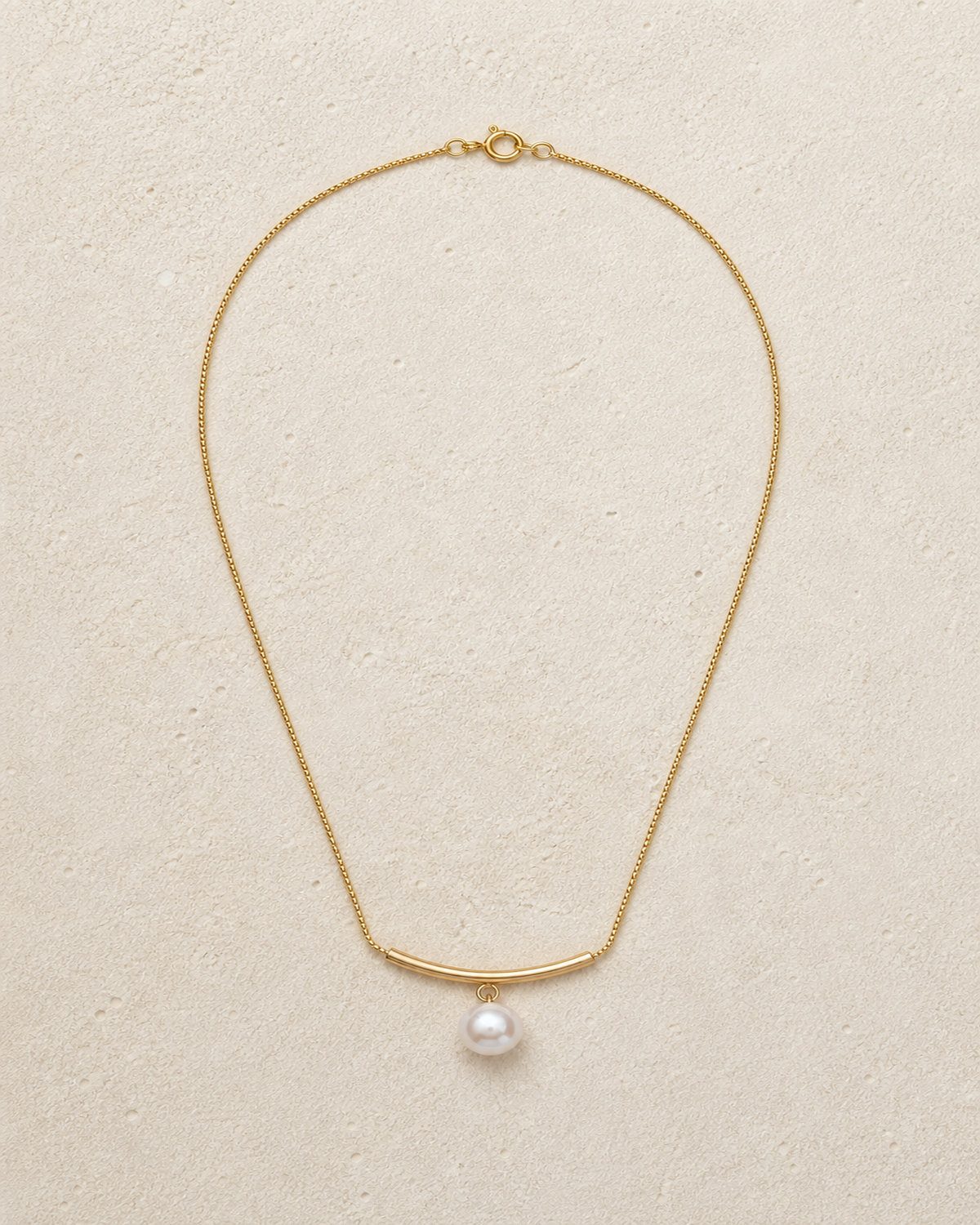 Arc pearl drop necklace laid on warm ivory limestone