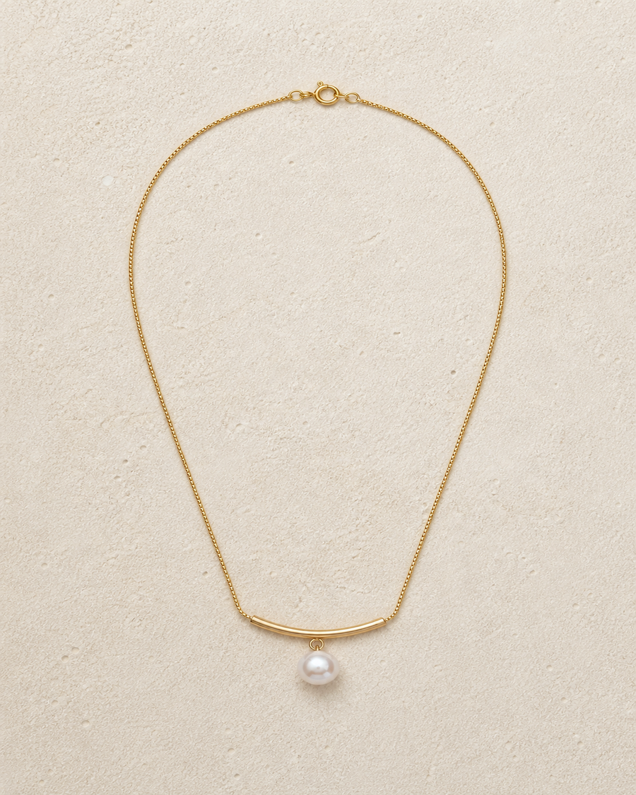 Arc pearl drop necklace laid on warm ivory limestone