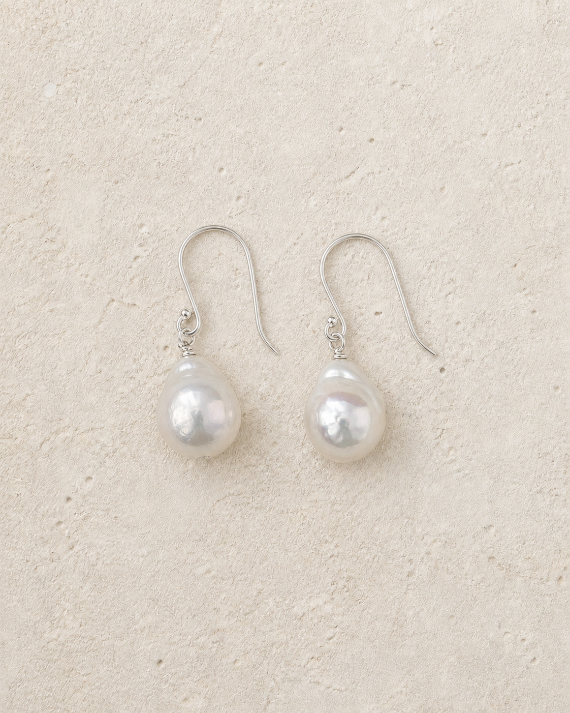 Drift Baroque Pearl Earrings resting on warm ivory stone