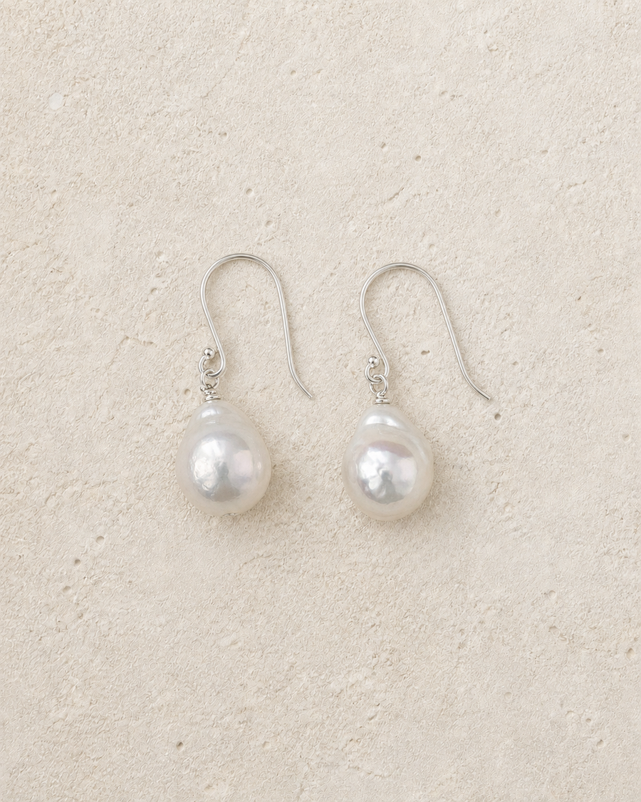 Drift Baroque Pearl Earrings resting on warm ivory stone