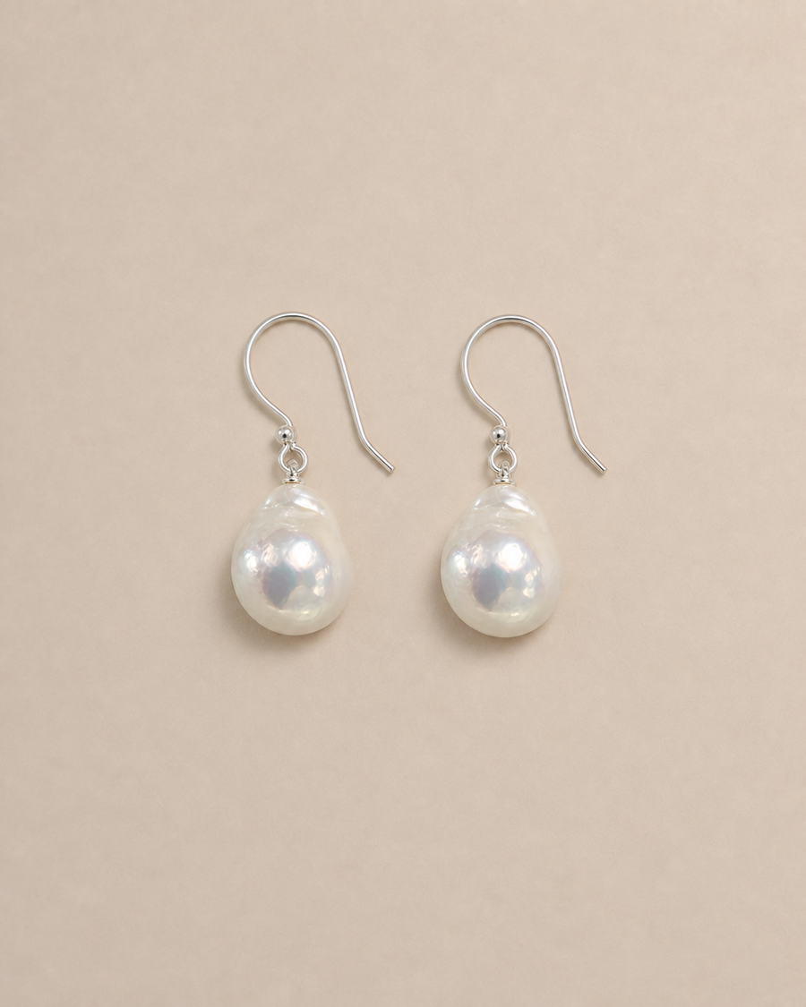 Drift Baroque Pearl Earrings laid flat with natural contact shadows on warm greige