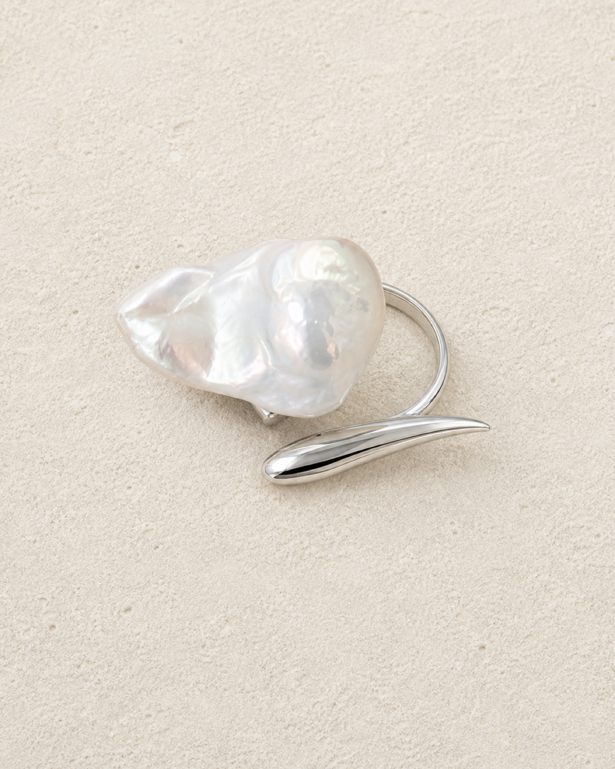 Veil Baroque Pearl Ring with an oversized irregular pearl and opposing silver leaf on warm ivory limestone