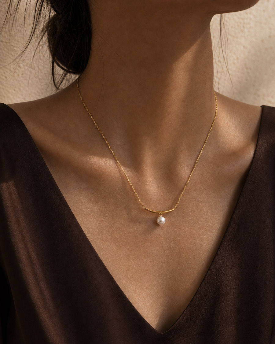 Arc Pearl Drop Necklace worn at the collarbone in a warm bronze and espresso editorial close-up